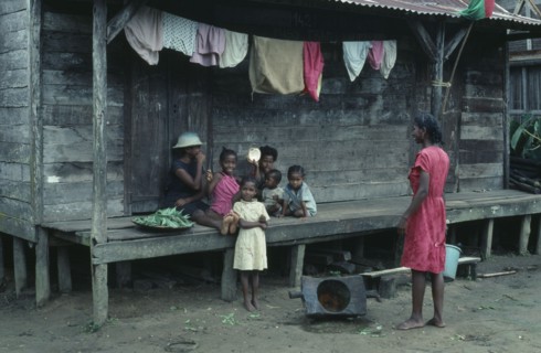 MADAGASCAR, Mananara, Local family sitting on raised wooden veranda of their home with line of