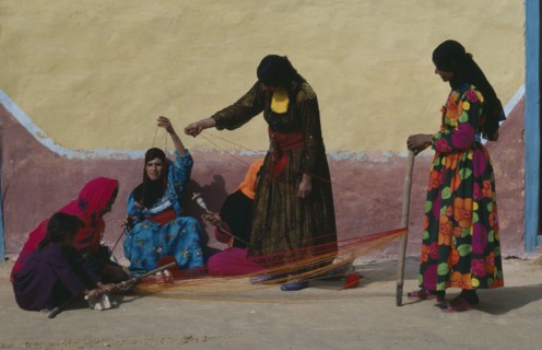 EGYPT, Western Desert, Bedouin, Group of Bedouin women in colourful dress weaving and spinning