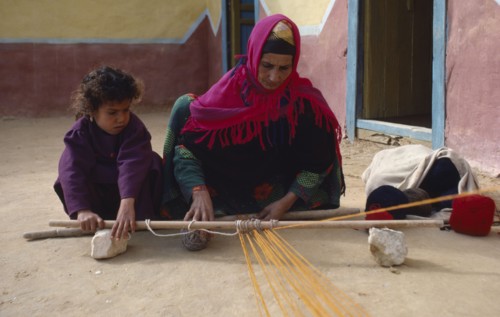 EGYPT, Western Desert, Bedouin, Bedouin woman and child in colourful dress weaving coloured yarn.