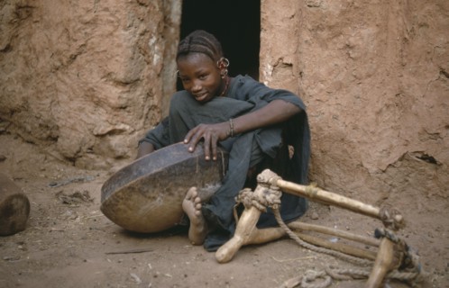 MAURITANIA, Oualata, Young girl cleaning bowl after meal with frame for carrying goods by donkey on