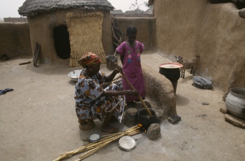 GHANA, Chereponi, "Woman cooking over open stove watched by young girl in small, walled yard with