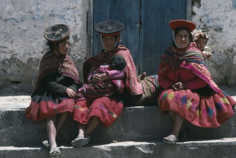 PERU, Cuzco, Ollantaytambo, Women carrying children in blanket slings resting in plaza after walk