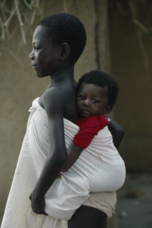 GHANA, Children, Child carrying sibling on her back wrapped in white cotton cloth.