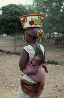 BURKINA FASO, People, Woman carrying baby in sling on her back and painted bowl on her head in area