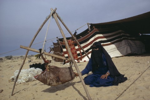 BEDOUIN, Family, Bedouin woman with baby in suspended cot made from animal hide with tent behind.
