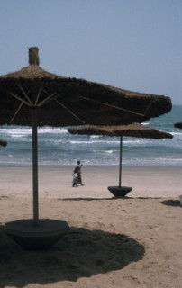 GAMBIA, Landscape , Beach, Beach with straw sun shades and a woman with children walking along the