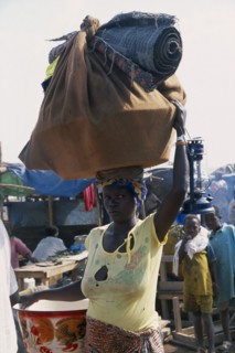 GUINEA, Kissidougou, Camp for Sierra Leonean Refugees. Woman carrying sack on her head arriving in