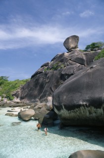 THAILAND, Koh Similan  , Sail Rock, A couple walking in the water at the base of the large rocks.