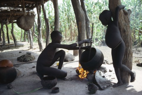 SUDAN, Tribal People, Dinka children cooking over open fire beneath house raised above ground level