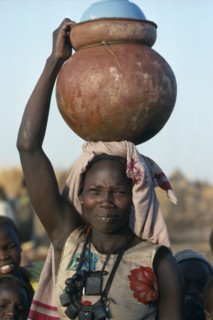 SUDAN, Momei Settlement, Chadian refugee carrying water pot on her head in camp near El Geneina