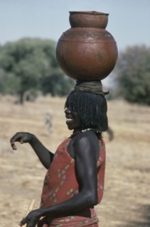 SUDAN, Habila Settlement, Laughing Chadian refugee woman carrying water pot on her head.