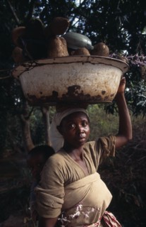 GHANA, People, Women, Portrait of young woman carrying bowl of yams on her head and baby in sling