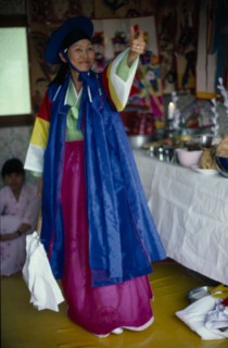 SOUTH KOREA, Religion, Shamanism, Female Shaman with arm raised in air at a funeral wearing