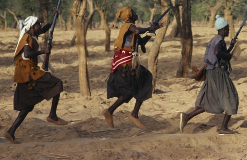 MALI, Ceremony, Dogon funeral dance.  Dancers carrying rifles leaping in line.