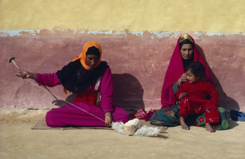 EGYPT, Western Desert, Settled Bedouin woman spinning wool with older woman and child sitting