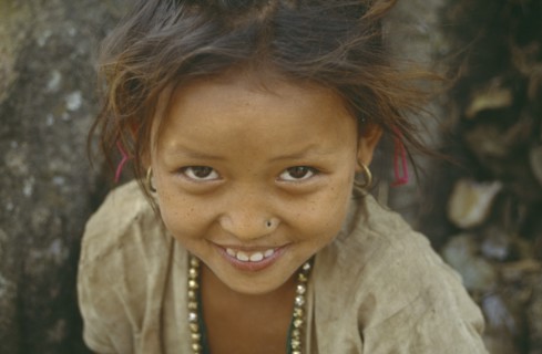 NEPAL, Dhankuta, Head and shoulders portrait of smiling young girl looking up to camera.