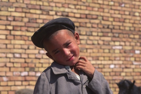 CHINA, Xinjiang Province, Kashgar, Portrait of young Tajik boy standing in front of brick wall