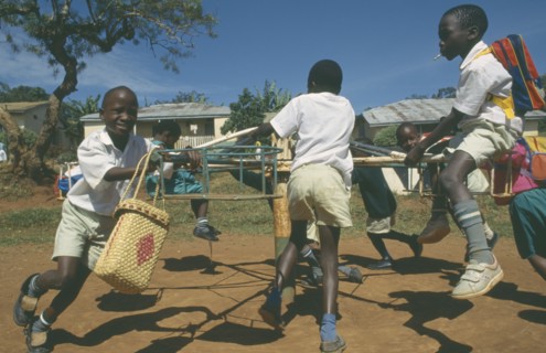 UGANDA, Mengo, Primary school children playing on roundabout. Young boy smoking cigarette.