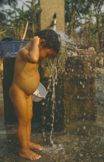 LAOS, Hygiene, Washing, Young Hmong girl washing under stand pipe in Hmong returnee villages for