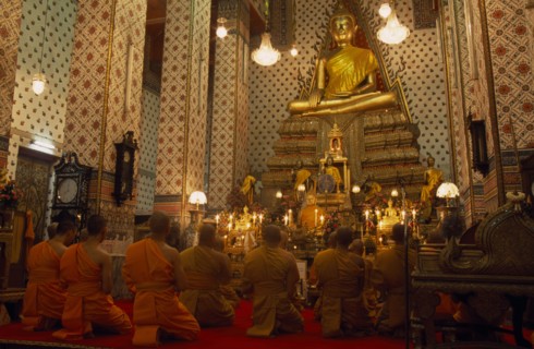 THAILAND, Bangkok, "Monks pray, kneeling down in front of large golden Buddha at Wat Arun. The