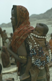 ETHIOPIA, Children, Carrying, Danakil tribeswoman carrying baby on her back in sling decorated with