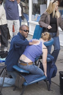 ENGLAND, East Sussex, Brighton, Masseur performing massage in East Street on a woman customer sat