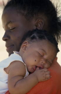WEST INDIES, St Lucia, Portrait of young mother holding baby girl asleep on her shoulder with thumb