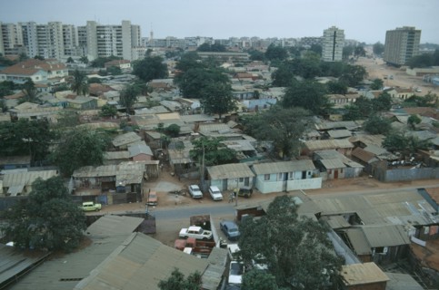 ANGOLA, Luanda, Cars parked next to houses along a road with high rise apartment blocks in the
