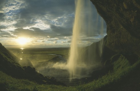 ICELAND, Seljalandfoss, View from behind waterfall in low golden sunlight through drifting cloud.