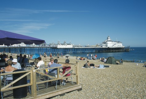 ENGLAND, East Sussex, Eastbourne, Beach cafe with people sat on chairs under parasols infront of