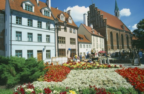 LATVIA, Riga, Church of St John beside town housing with colourful flowerbeds in the foreground on