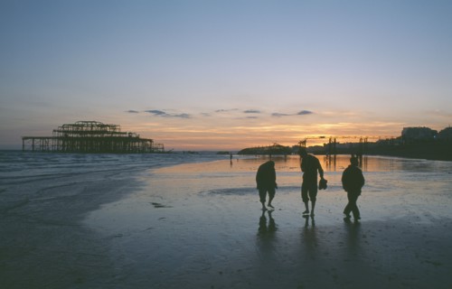ENGLAND, East Sussex, Brighton, The ruined West Pier at sunset with low tide and a group of people