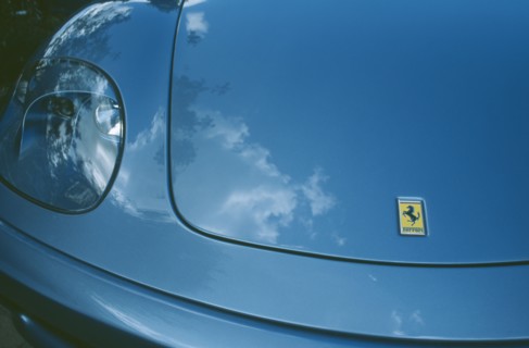 TRANSPORT, Road, Cars, Detail of blue Ferrari emblem and front light with clouds reflected in