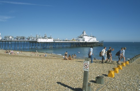ENGLAND, East Sussex, Eastbourne, View across shingle beach towards pier with a group of people