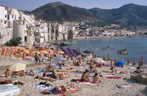 ITALY, Sicily, Palermo, Cefalu. View across busy sandy beach with sunbathers on sand and swimming