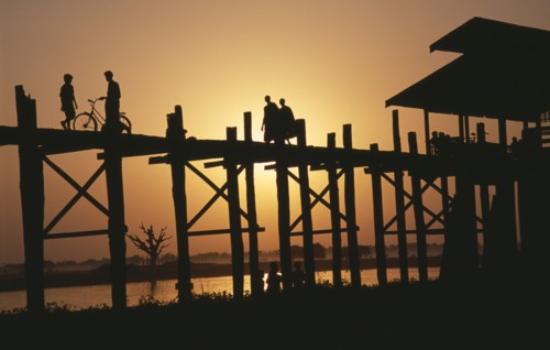 MYANMAR, Amarapura, "U Bein Bridge near Mandalay at sunset with silhouetted figures of monks, child