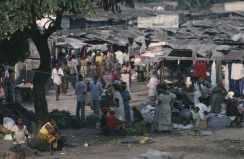 CONGO, Kinshasa, Busy market scene with people and lines of stalls with corrugated iron rooftops.
