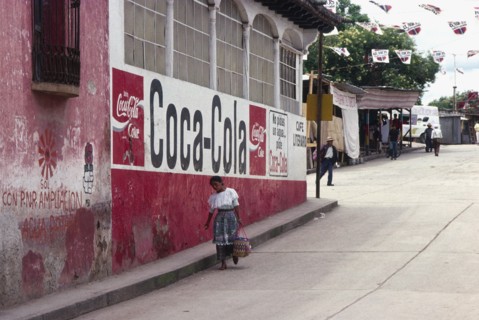 GUATEMALA, Solola, Indigenous woman walks down street past a Coca Cola street sign.