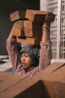 MYANMAR, Mandalay, Female construction worker carrying bricks on her head.