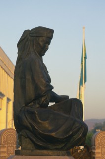 KAZAKHSTAN, Almaty, Stutue of person sat down and a flag pole behind.
