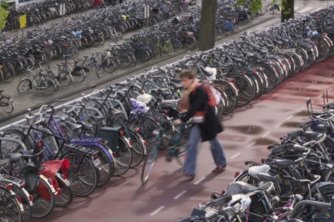 HOLLAND, North, Amsterdam, Bicycles parked near the Central Station and a person pushing one along.