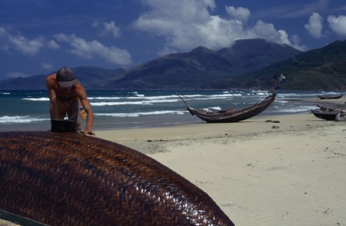 VIETNAM, Lang Co, Man sealing hull of overturned fishing boat with other boats pulled up onto sand