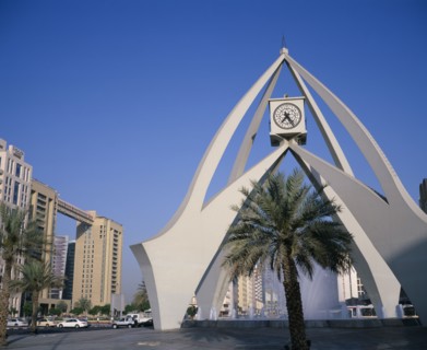 UAE, Dubai, Dubai Clock Tower.  Modern sculptural structure with pool and fountains below and palm