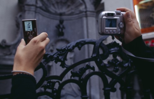 BELGIUM, Brabant, Brussels, Cropped view of visitors to the Manneken-Pis statue holding up digital