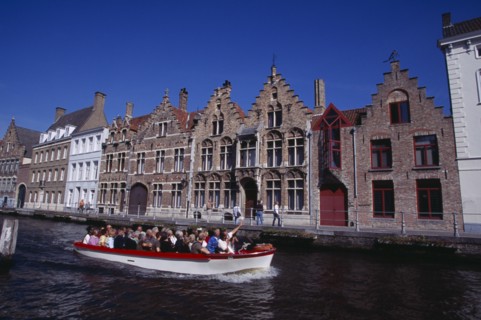 BELGIUM, West Flanders, Bruges, Tourist boat on canal with guide pointing out traditional waterside