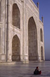 INDIA, Uttar Pradesh, Agra, Taj Mahal.  Part view of white marble exterior with woman sitting on