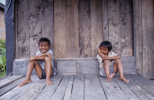 INDONESIA, Sumatra, Children, Two laughing children sitting on wooden floor of building.
