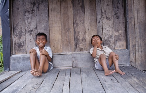 INDONESIA, Sumatra, Children, Two laughing children sitting on wooden floor of building.