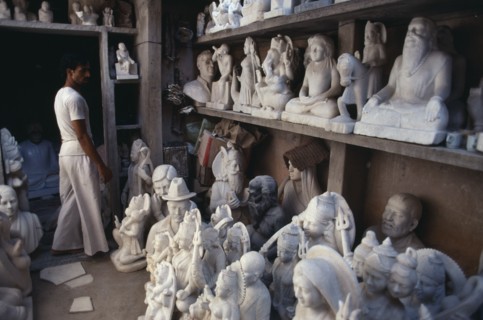 INDIA, Rajasthan, Jaipur, Marble carver in workshop with shelves of statues.