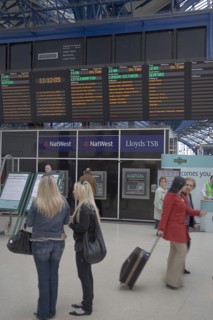 ENGLAND, East Sussex, Brighton, Passengers waiting by noticeboard at the central railway station.